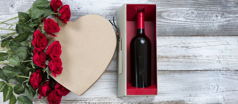 Happy Valentines Day celebration with wine, red roses and a heart shaped gift box on white rustic wood 