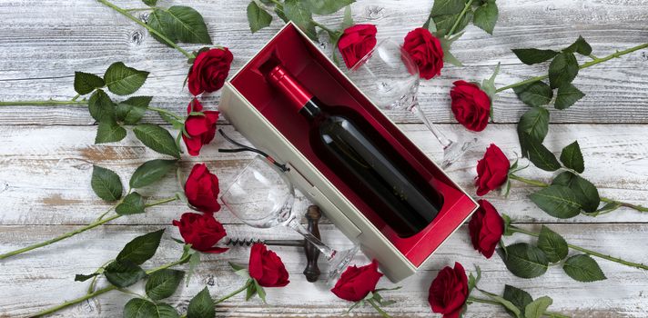 Happy Valentines Day celebration with red roses and a bottle of wine on white rustic wooden background   