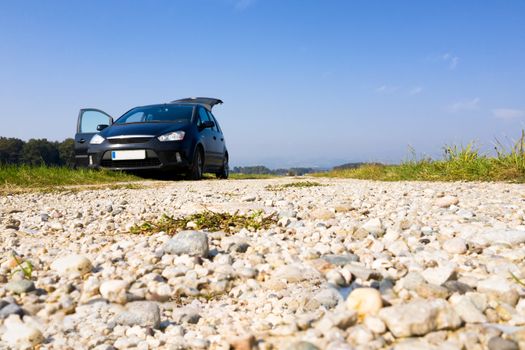 Black van parked on gravel road, low angle, copyspace, trunk and door open, nobody, offroad, camping in nature, plain blue sky in background