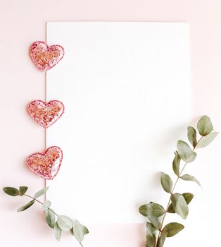 Background with copy space blank on pink background with pink glittered hearts, eucalyptus branch. White paper top view, flat lay, minimal style. Moke up card