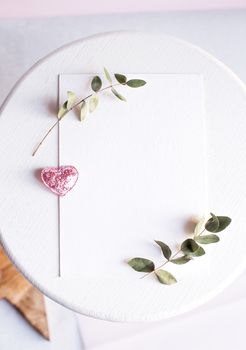 Background with copy space blank on table with glitter heart, eucalyptus branch, flowers and leafs. White paper top view, flat lay, minimal style. Moke up card