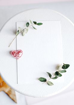 Background with copy space blank on table with glitter heart, eucalyptus branch, flowers and leafs. White paper top view, flat lay, minimal style. Moke up card