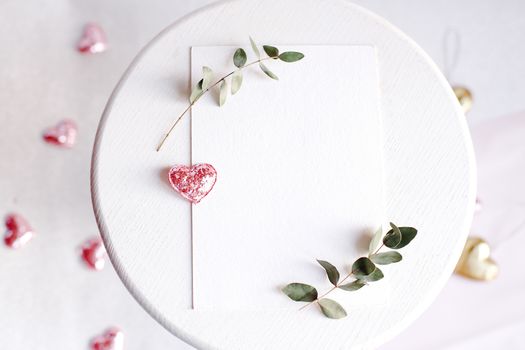 Background with copy space blank on table with glitter heart, eucalyptus branch, flowers and leafs. White paper top view, flat lay, minimal style. Moke up card