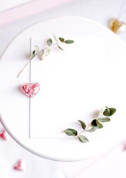 Background with copy space blank on table with glitter heart, eucalyptus branch, flowers and leafs. White paper top view, flat lay, minimal style. Moke up card