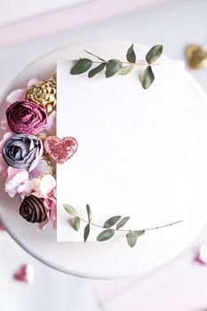 Background with copy space blank on table with glitter heart, eucalyptus branch, flowers and leafs. White paper top view, flat lay, minimal style. Moke up card