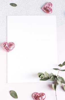 Background with copy space blank on table with glitter heart, eucalyptus branch, flowers and leafs. White paper top view, flat lay, minimal style. Moke up card