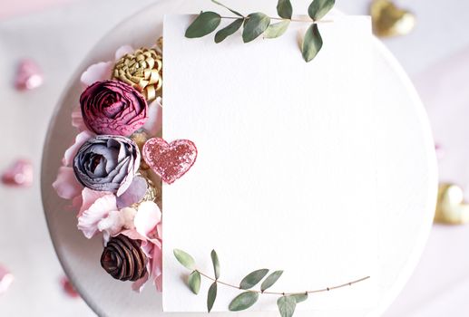 Background with copy space blank on table with glitter heart, eucalyptus branch, flowers and leafs. White paper top view, flat lay, minimal style. Moke up card