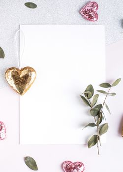 Background with copy space blank on table with glitter heart, eucalyptus branch, flowers and leafs. White paper top view, flat lay, minimal style. Moke up card