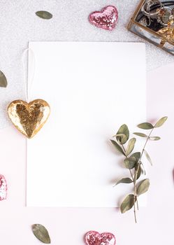 Background with copy space blank on table with glitter heart, eucalyptus branch, flowers and leafs. White paper top view, flat lay, minimal style. Moke up card