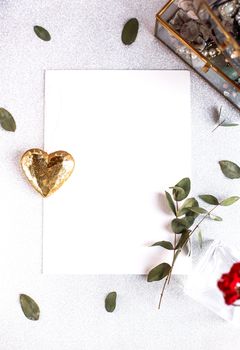 Background with copy space blank on table with glitter heart, eucalyptus branch, flowers and leafs. White paper top view, flat lay, minimal style. Moke up card