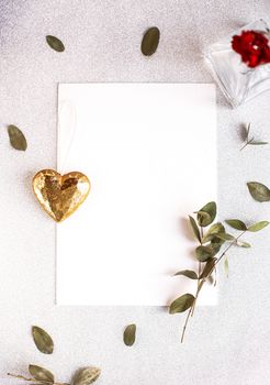 Background with copy space blank on table with glitter heart, eucalyptus branch, flowers and leafs. White paper top view, flat lay, minimal style. Moke up card