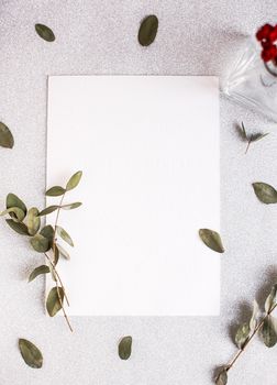 Background with copy space blank on table with glitter heart, eucalyptus branch, flowers and leafs. White paper top view, flat lay, minimal style. Moke up card