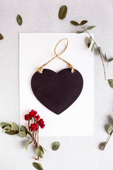 Background with copy space blank on table with black heart, eucalyptus branch, roses flowers and leafs. White paper top view, flat lay, minimal style. Moke up card