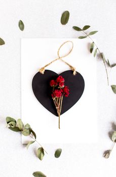 Background with copy space blank on table with black heart, eucalyptus branch, roses flowers and leafs. White paper top view, flat lay, minimal style. Moke up card