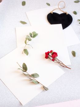 Background with copy space blank on table with black heart, eucalyptus branch, roses flowers and leafs. White paper top view, flat lay, minimal style. Moke up card