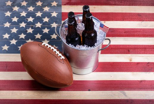 Top view of American football and bucket of ice cold beer on rustic wooden boards with painted USA Flag.