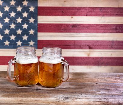 Two pint jars filled with beer with vintage wooden USA flag in background.