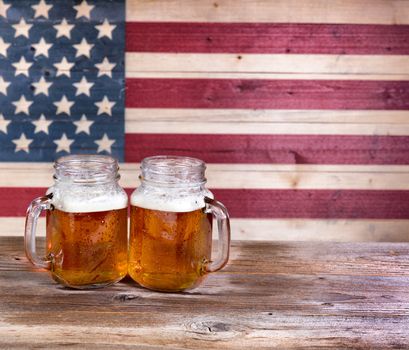 Two pint jars filled with beer with vintage wooden USA flag in background.