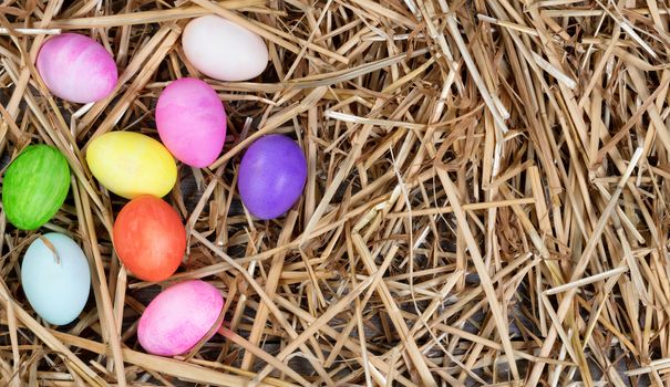 Colorful Easter egg decorations forming left hand border on natural straw and wood. 
