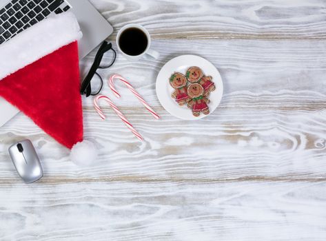 Overhead view of a holiday office workplace desk with cookies and coffee and a Santa cap on laptop keyboard.  