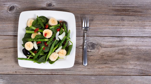 Fresh salad with spinach, asparagus, olive, banana, onion, olives, and cranberries. Overhead view. 