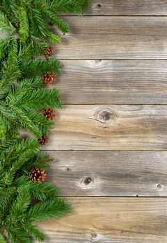 Christmas border with pine tree branches, and cones on rustic wooden boards. Layout in vertical format.  