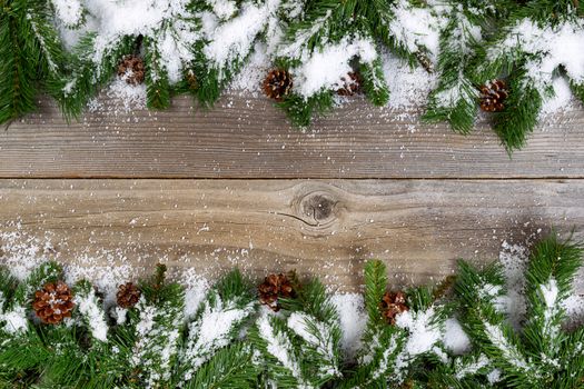Christmas border, top and bottom of frame, with pine tree branches, cones and snow on rustic wooden boards. Layout in horizontal format.  