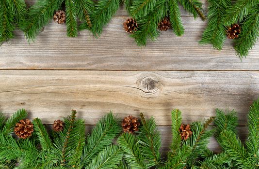 Christmas border, top and bottom of frame, with pine tree branches and cones on rustic wooden boards. Layout in horizontal format.  