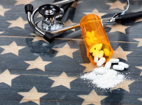 Close up front view of prescription bottle with generic opioid pain killer tablets. Rustic USA flag and medical stethoscope in background for drug addiction concept in America  