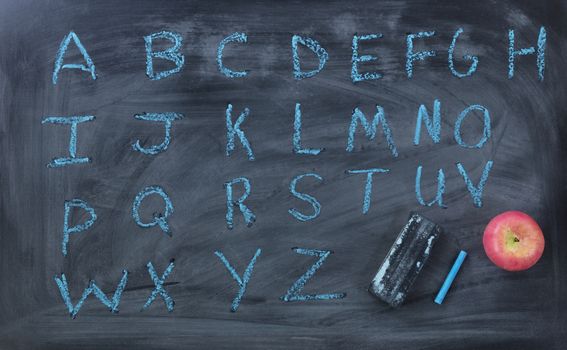 Alphabet blue letters with eraser and apple on blackboard 