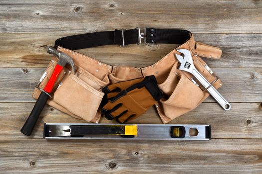 Traditional leather tool belt with tools on rustic wooden floor.