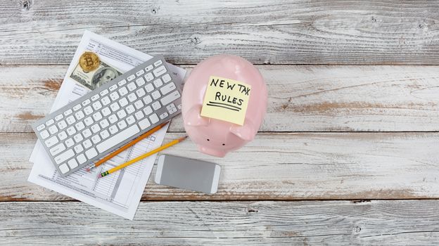 Overhead view of income tax forms with new rule changes and piggy bank on white rustic desk 