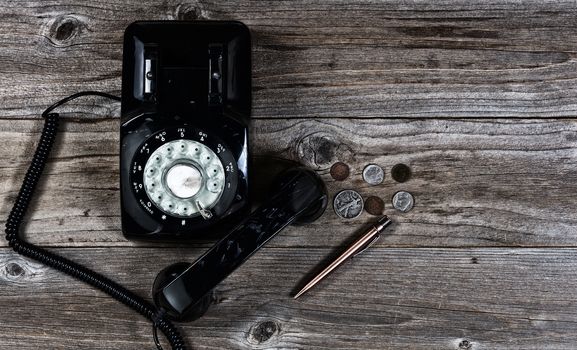 Flat layout of vintage telephone, pen and coins on rustic wood with lighting effects applied. 