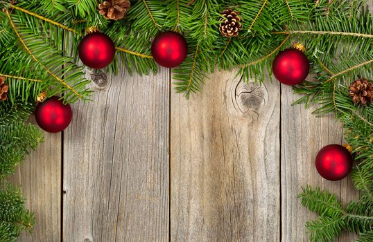 Real Fir tree branches and cones with red ornaments on rustic wooden boards forming border. Christmas season concept.