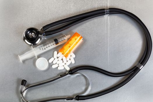 Flat view of painkiller pills with open bottle, stethoscope and syringe. Opioid epidemic concept.