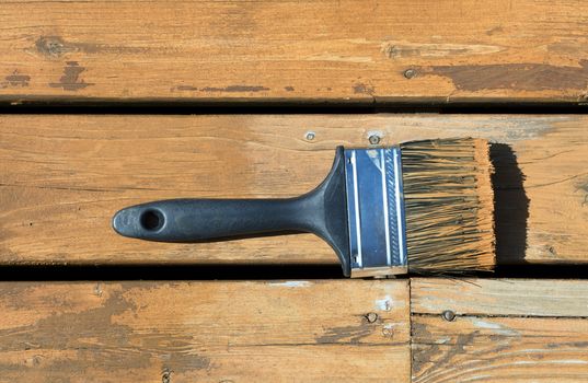 Used paintbrush filled with wood stain on a natural cedar wooden deck 