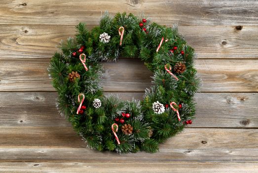 Christmas wreath decorated with pine cones, candy canes, and red berries on rustic wooden boards. 