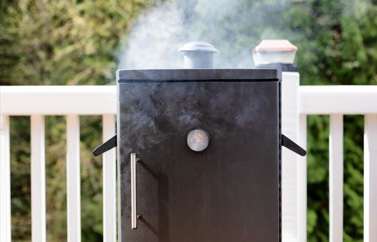 Close up of a cooking smoker with woods in background