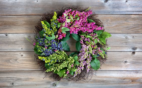 Colorful artificial wreath made of flowers and leaves on vintage wood background 