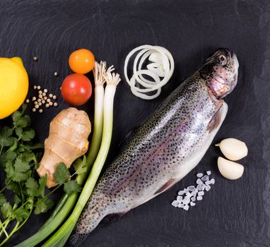 Overhead view of whole fish with various herbs, vegetables, and spices on black natural state. Healthy food concept. 