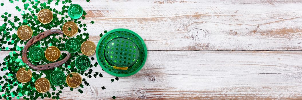 Bright green shamrock with gold coins, hat and rusty horseshoe for Saint Patrick Day on white rustic wooden background 