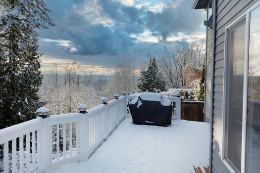 Home outdoor deck closed for the winter season with snow on BBQ cooker cover 