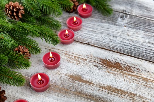 Traditional Christmas holiday candles and evergreen branches with on white rustic wood background 