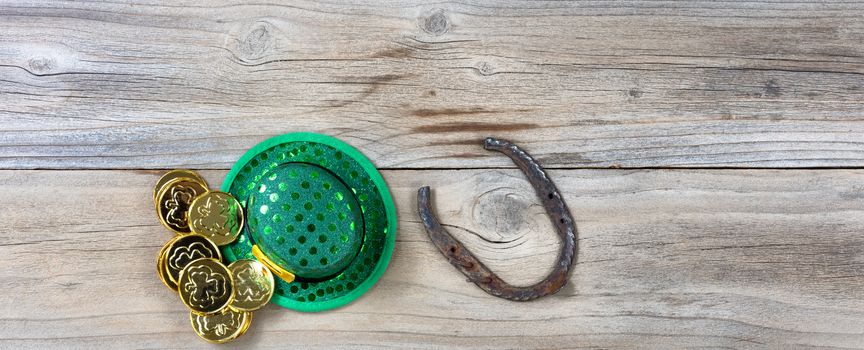 Lucky green hat, horseshoe and gold coins for St Patrick on rustic wooden boards in overhead view 