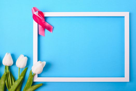 Breast cancer month concept, flat lay top view, pink ribbon and Tulip Flower with photo frame on blue background with copy space for your text