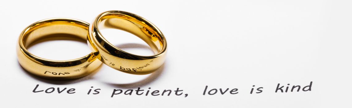 Two golden wedding rings on Holy bible book phrase close up, love is patient, love is kind