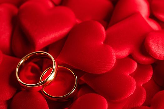 Two golden wedding rings on red satin hearts background