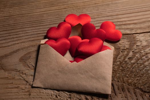 Valentine day love letter, envelope with red hearts heap spread on wooden background.