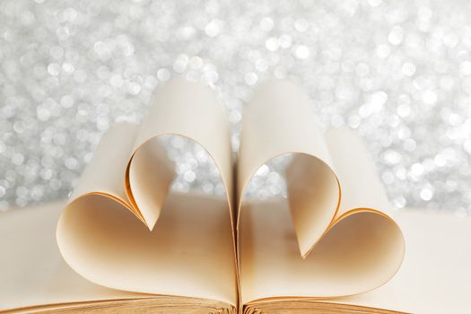 Pages of open book rolled in heart shape on glitter background