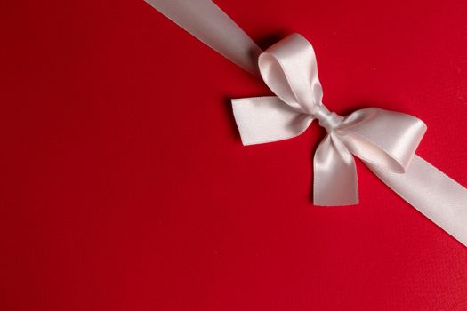 White satin ribbon bow on red paper background